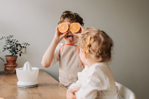 Free Kids having fun with oranges, making silly faces in a cozy indoors setting. Stock Photo