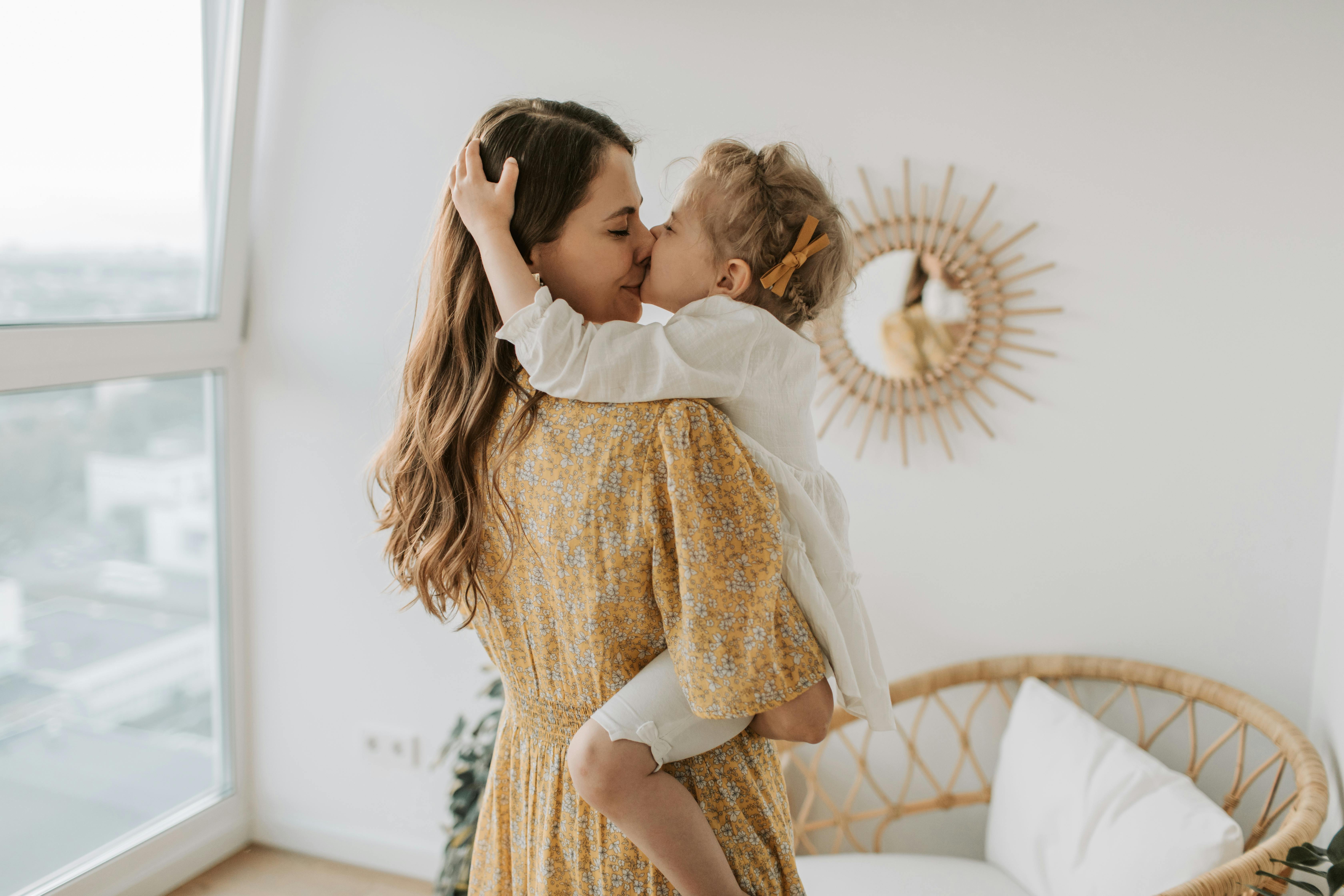 woman in yellow floral dress kissing girl in white long sleeves shirt