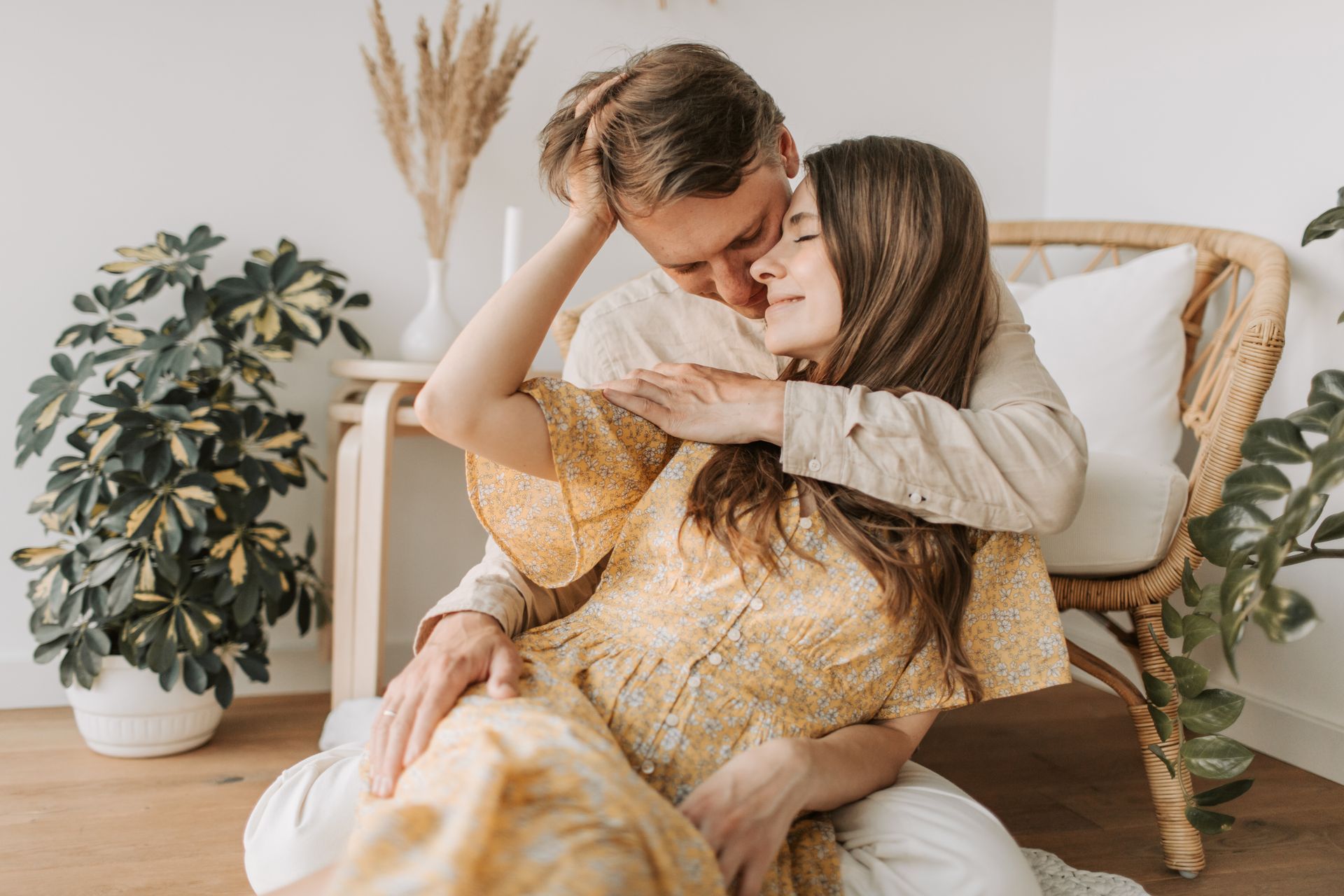 A loving couple embracing in a cozy indoor setting with natural decor and soft lighting.