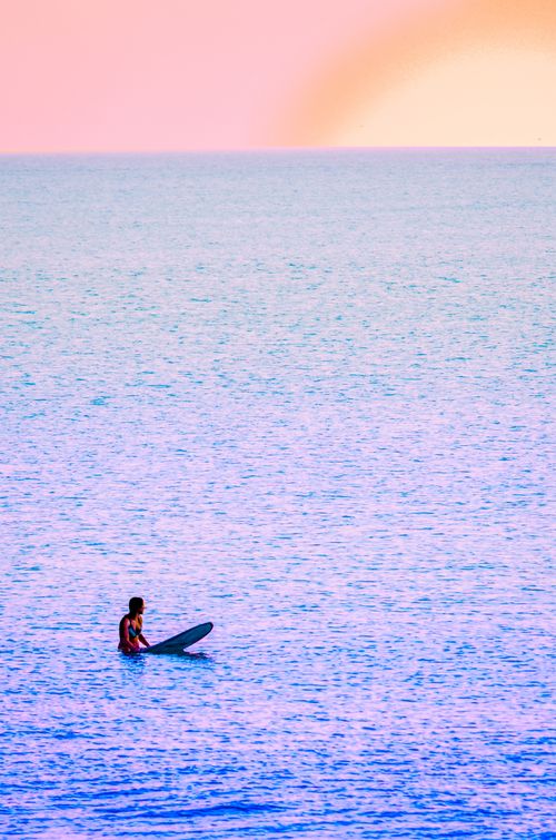 Free A lone surfer on a surfboard waits for waves in the calm ocean at sunset. Perfect serenity. Stock Photo