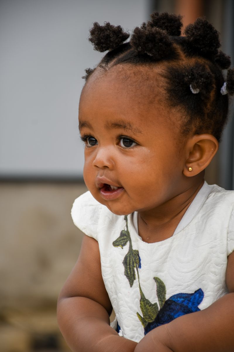 A Black toddler girl with afro puffs and a white floral dress, the age group at highest risk for lead exposure and the age the blood lead test matters most.