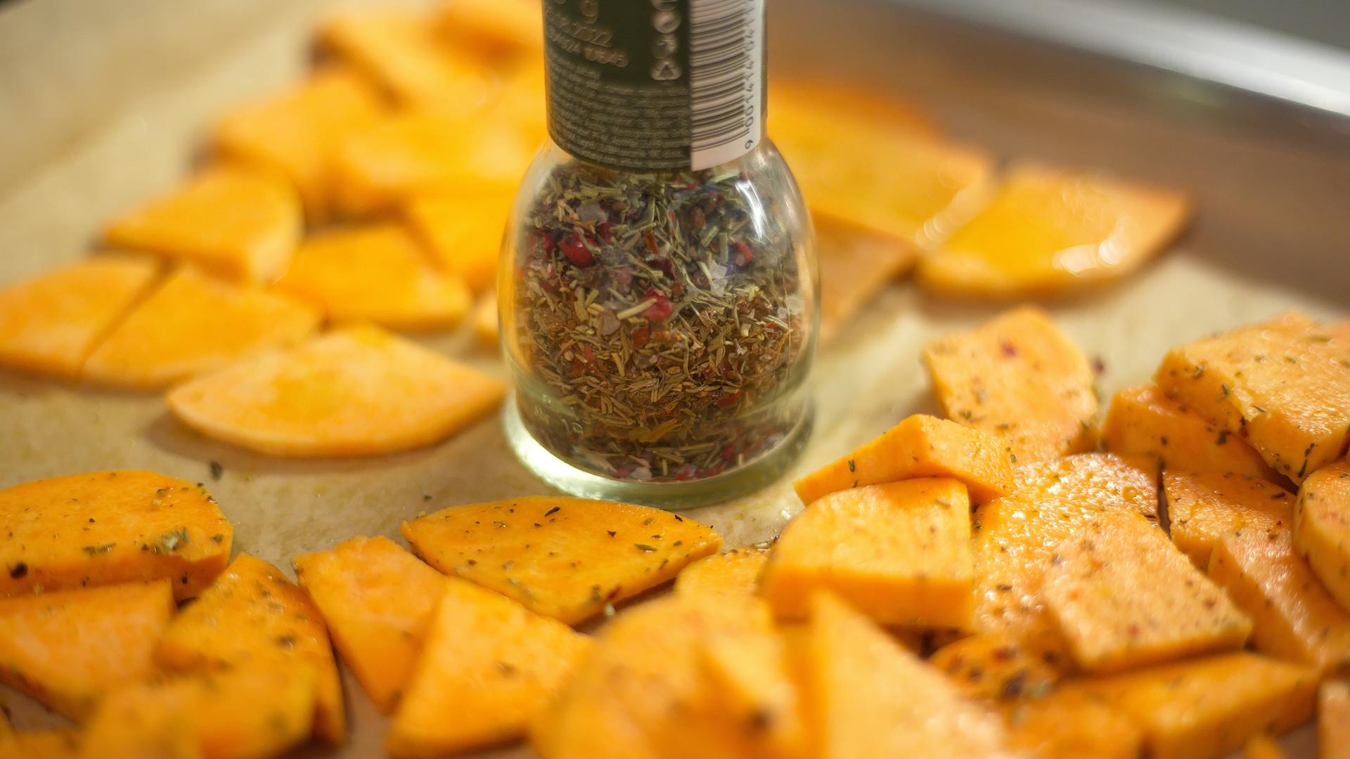 Close-up view of freshly seasoned sweet potato slices with spice vial, perfect for food enthusiasts.