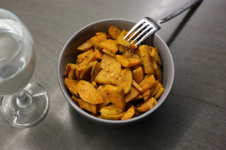 A sheet pan of golden-brown roasted white sweet potato cubes flecked with rosemary and garlic, with a small bowl of fresh chives beside it.