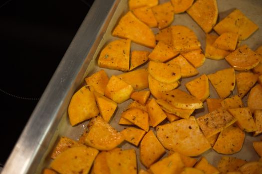 From above of appetizing sliced fried potatoes with spices scattered on oven pan in kitchen