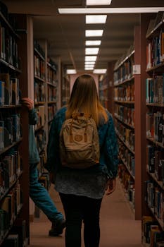 A young woman with a backpack navigates through bookshelves in a library corridor.