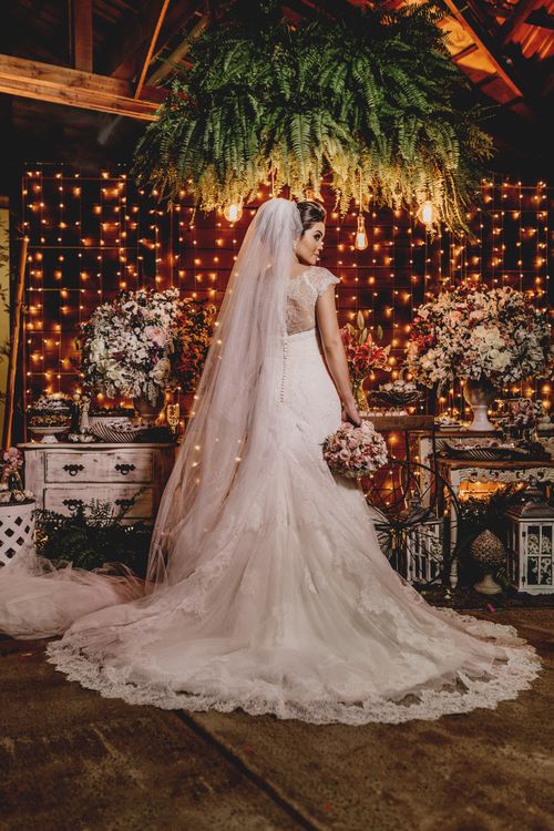 Free Back view of gorgeous young bride in luxurious white dress and veil standing near floral decorations with bouquet in hand and looking away Stock Photo