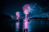 城市海滨上空，壮观的烟花表演在水面倒影和一座桥梁的映衬下上演