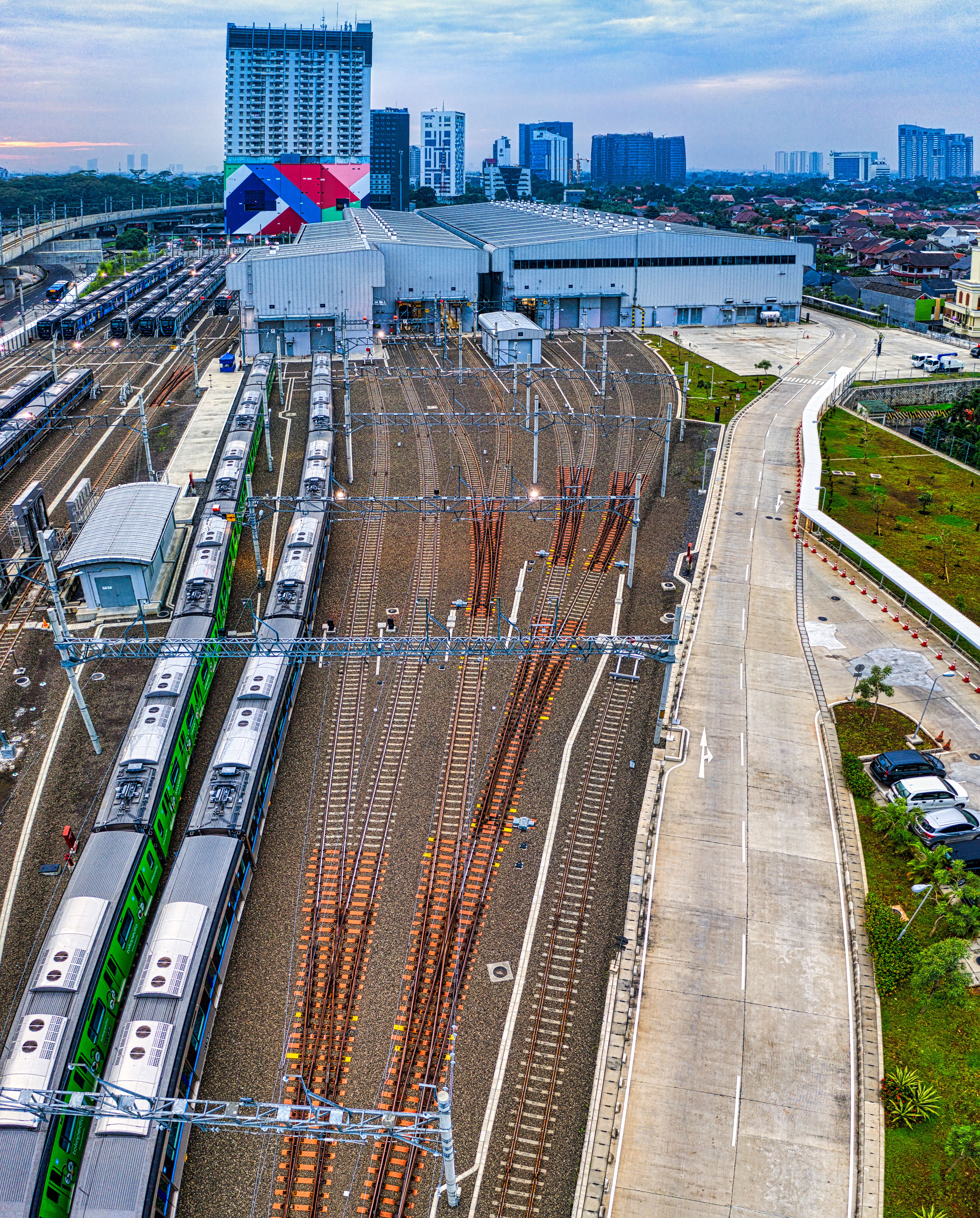 Aerial view of Jakarta train station with trains and cityscape in the background, showcasing urban transportation.