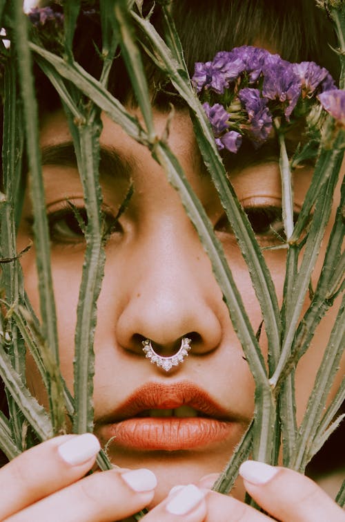 Free A Woman Wearing a Nose Jewel Holding a Plant with Flower Near Her Face Stock Photo