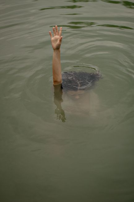 Fotomural Una persona sumergida en el agua levanta la mano pidiendo ayuda, evocando un sentido de urgencia y drama.