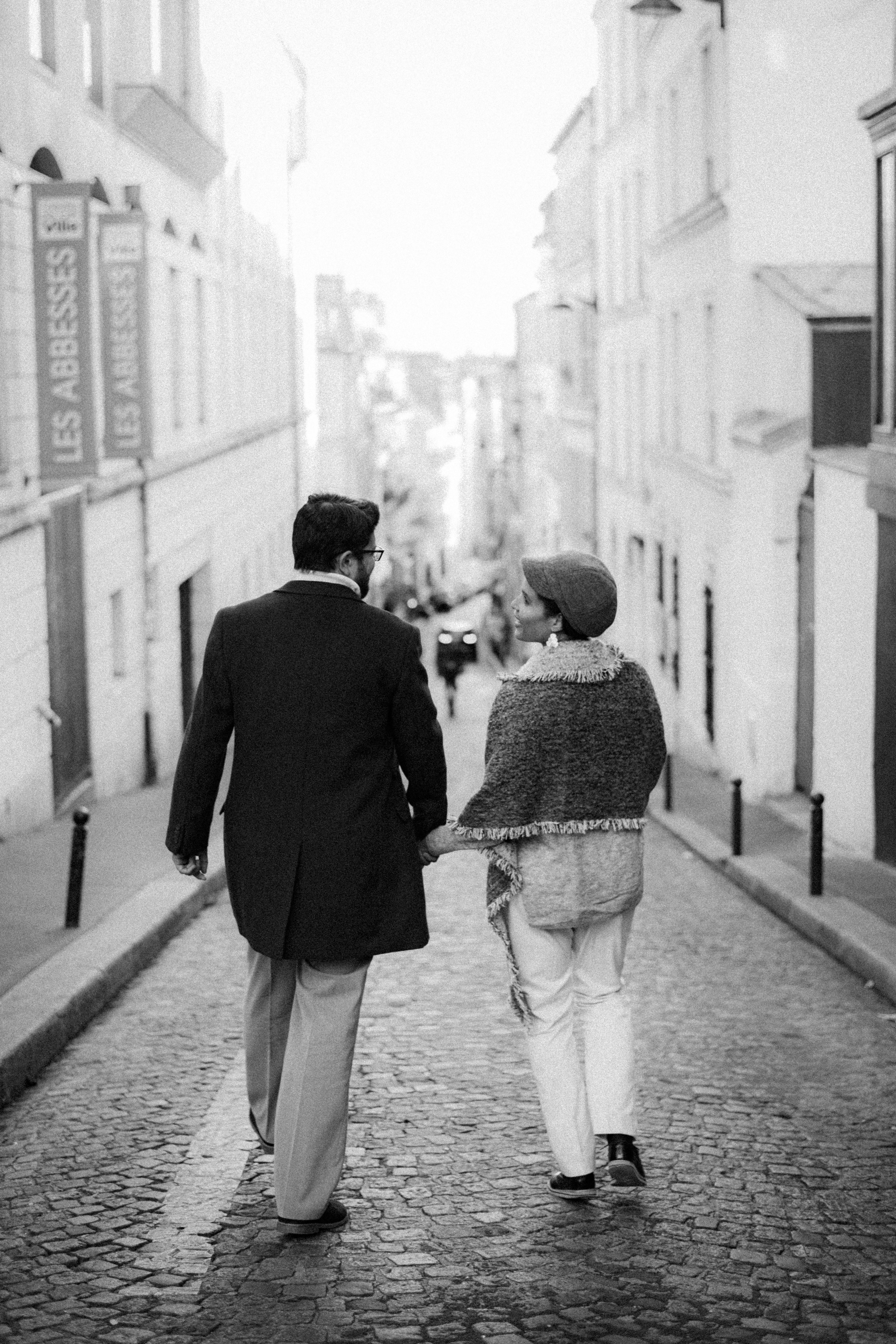 Stylish couple walking hand in hand down a cobblestone street in black and white.