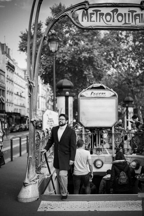 Man in Black Suit Standing on Sidewalk in Grayscale Photography