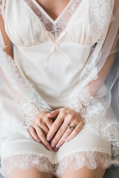 Close-up of a bride in lace gown with hands folded, highlighting elegance and style.