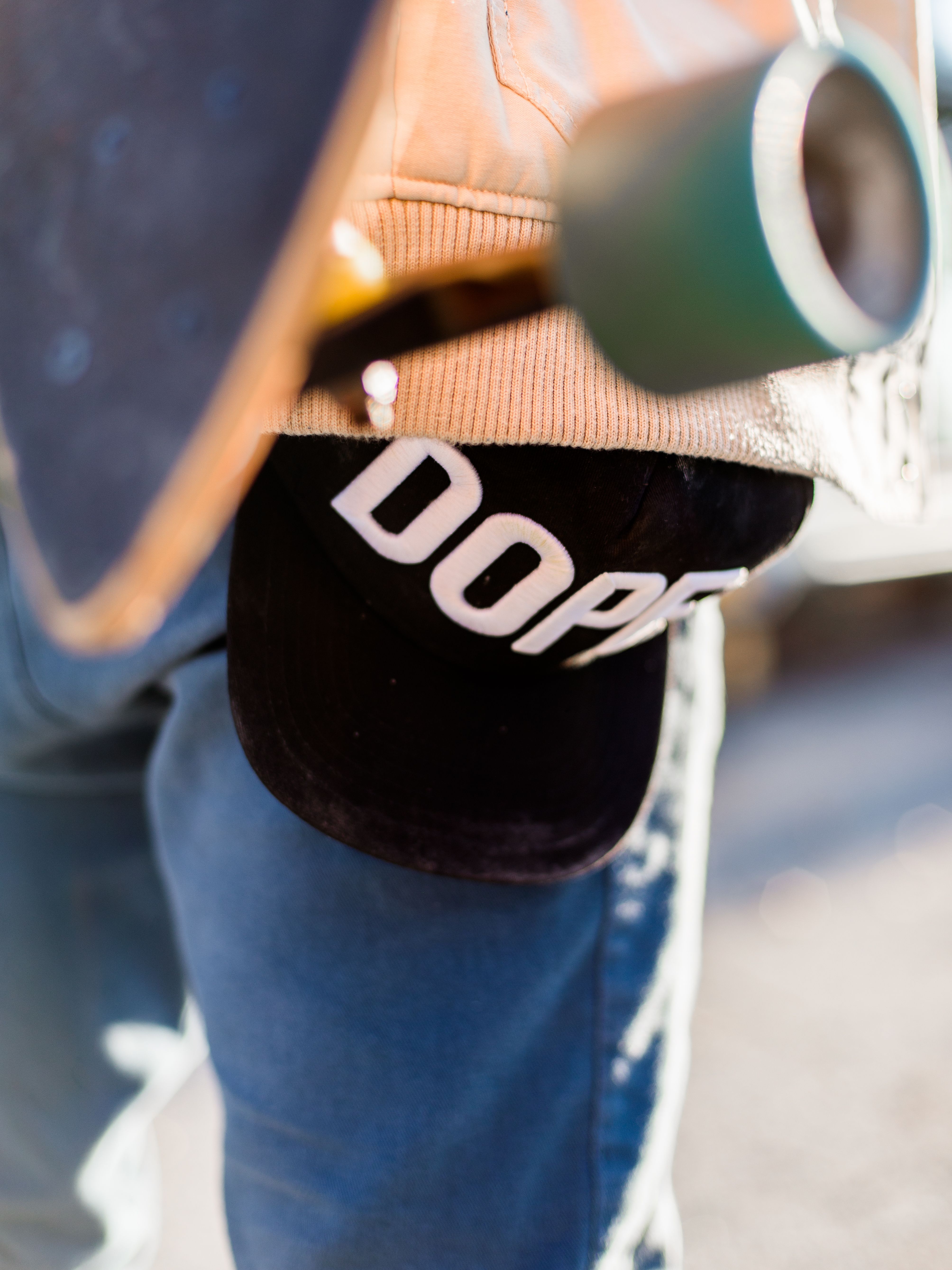 Close-up of skateboarder holding a 'DOPE' cap with a skateboard, emphasizing street style.