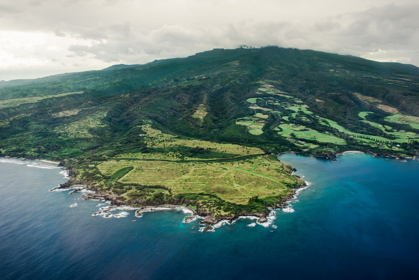 Green hills running down to the ocean under overcast sky on a quiet Hawaiian coast