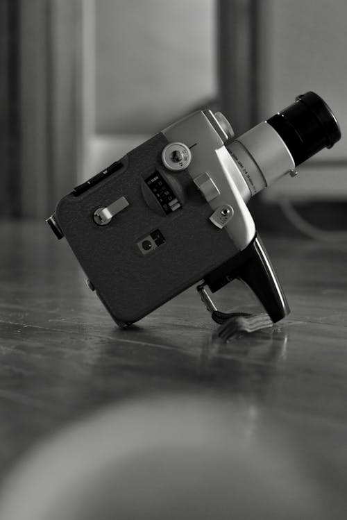 Black and white of old vintage video camera with long lens on glossy floor in room