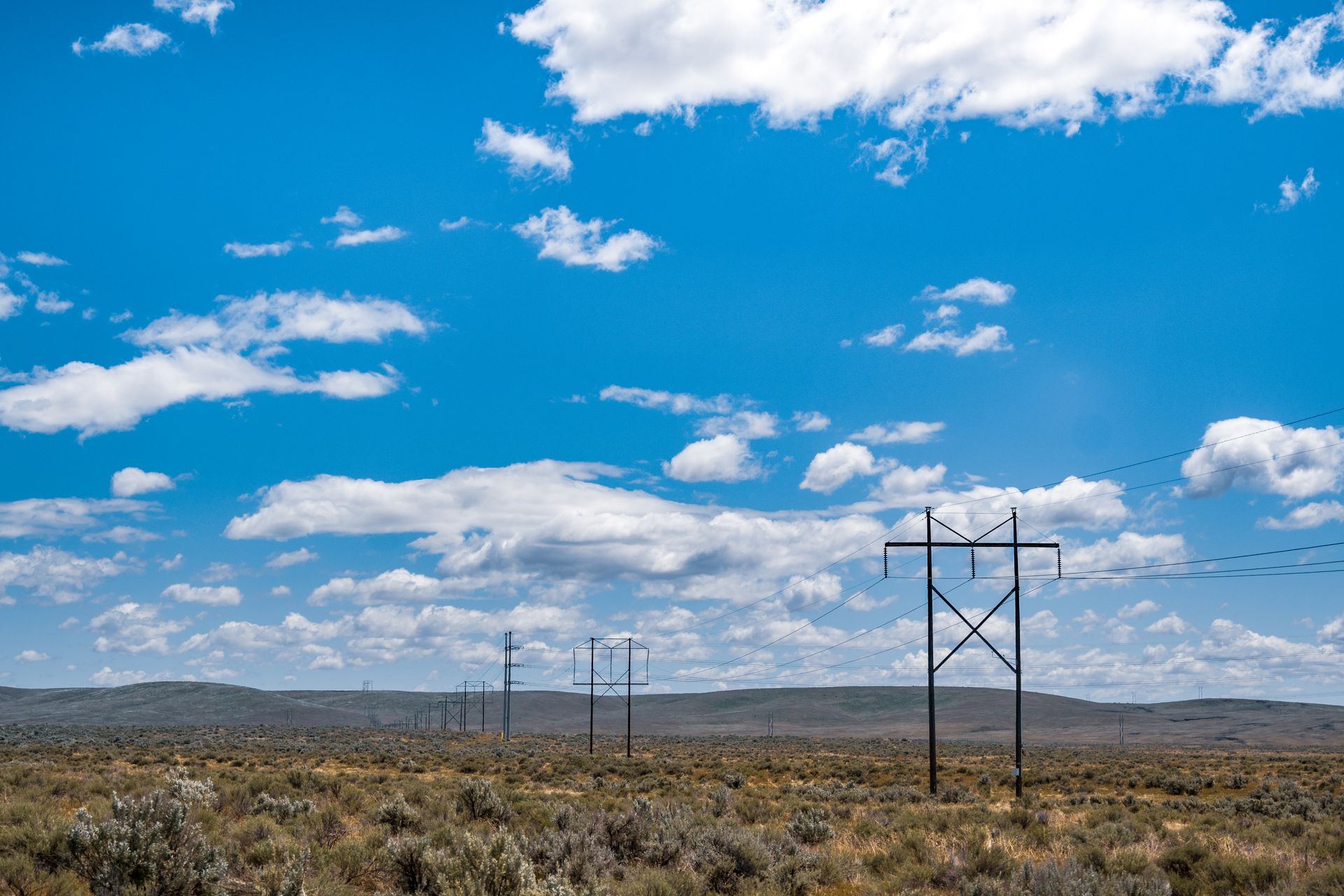Tranquil rural landscape with power lines under a blue sky with clouds.