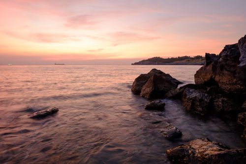 Free Peaceful sunset over the ocean with rocks and calm waters, creating a serene seascape. Stock Photo