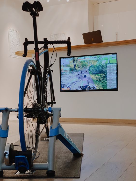 Home cycling setup with a bike on a rear-wheel trainer and a virtual cycling app open on the TV screen — illustrates the 5-step smart trainer installation