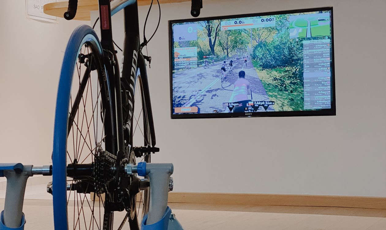 Home cycling setup with a bike on a rear-wheel trainer and a virtual cycling app open on the TV screen — illustrates the 5-step smart trainer installation