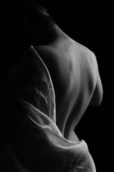 Elegant monochrome photo capturing the artistic silhouette of a woman's back with soft lighting and fabric.