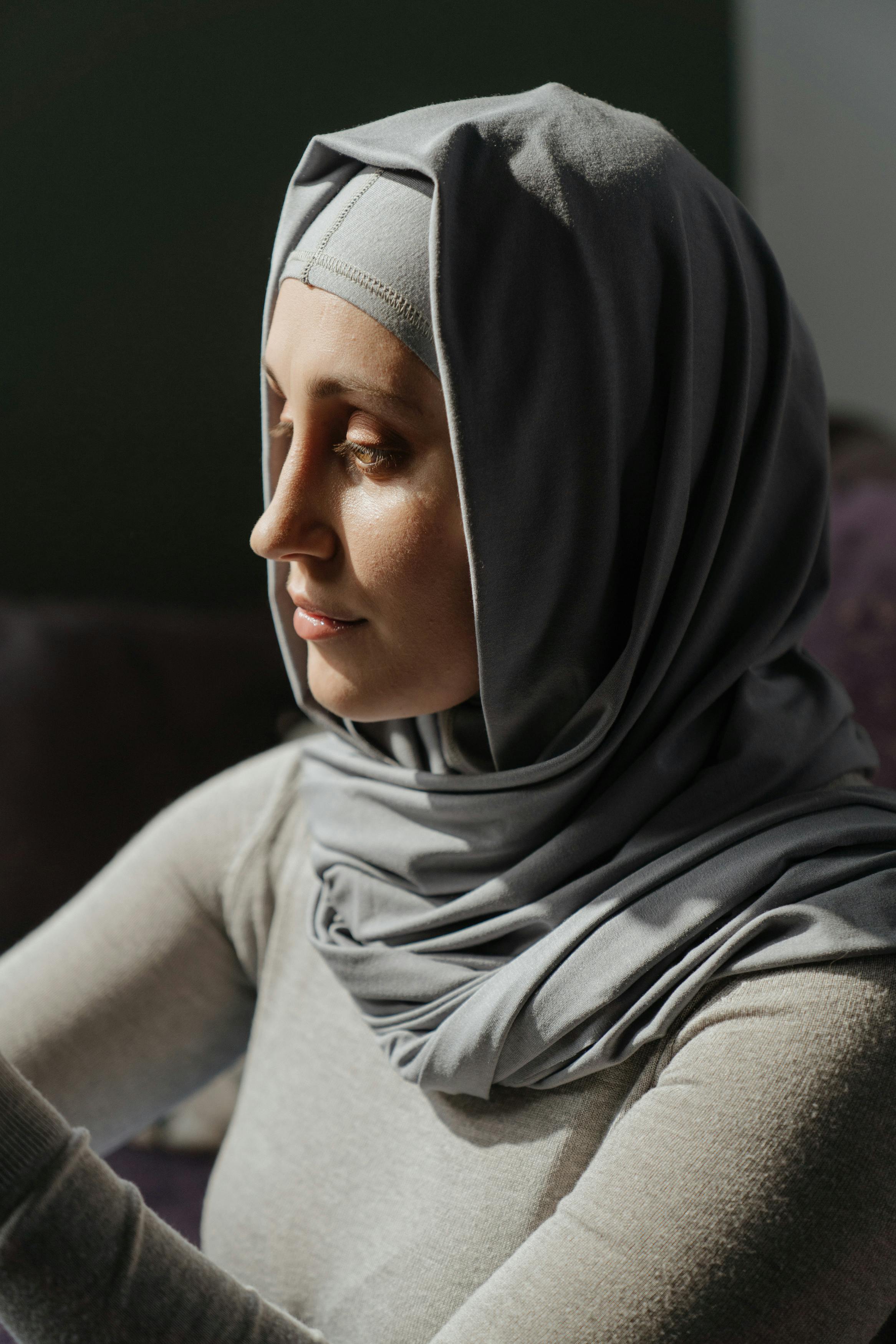 Woman in gray hijab and black leggings sitting on brown wooden