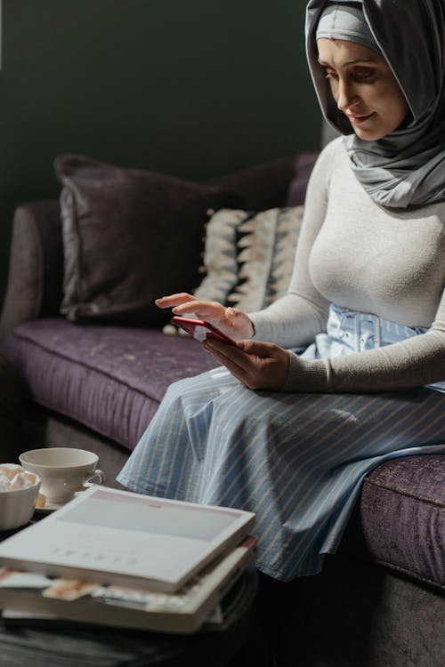 Free Woman in White Knit Sweater and Gray Pants Sitting on Couch Stock Photo
