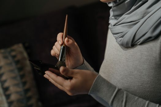 A woman wearing a hijab applies makeup using a brush indoors. Close-up shot.