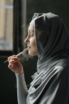 A serene profile shot of a woman in a hijab applying makeup indoors, illustrating beauty and self-love.