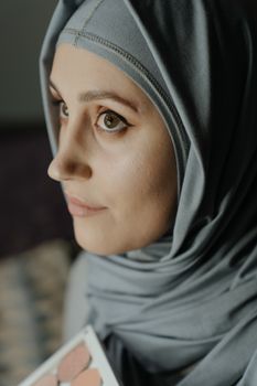 Close-up portrait of a woman in a hijab with elegant makeup indoors.