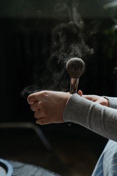 Close-up of hand using makeup brush indoors with powder dust effect.