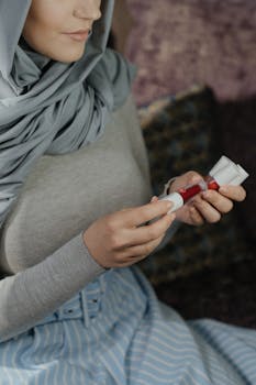A woman in a hijab carefully holds a lip gloss bottle, embodying a serene beauty routine.