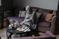 一名穿着传统服装的穆斯林妇女在舒适的客厅里用笔记本电脑工作