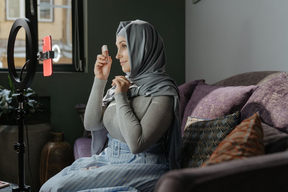 초보 블로거 필독: 애드센스 수익화 시작부터 성장까지 2 A woman in hijab applying makeup indoors, recording a tutorial with a smartphone and ring light.