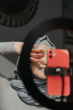 Muslim woman capturing a selfie indoors, showcasing henna art on her hands.