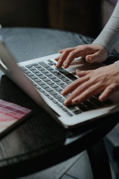 Close-up of woman's hands typing on a laptop keyboard indoors on a table.