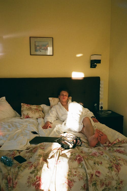 Full body of serious tourist of warm white bathrobe chilling in hotel room decorated with picture on yellow wall