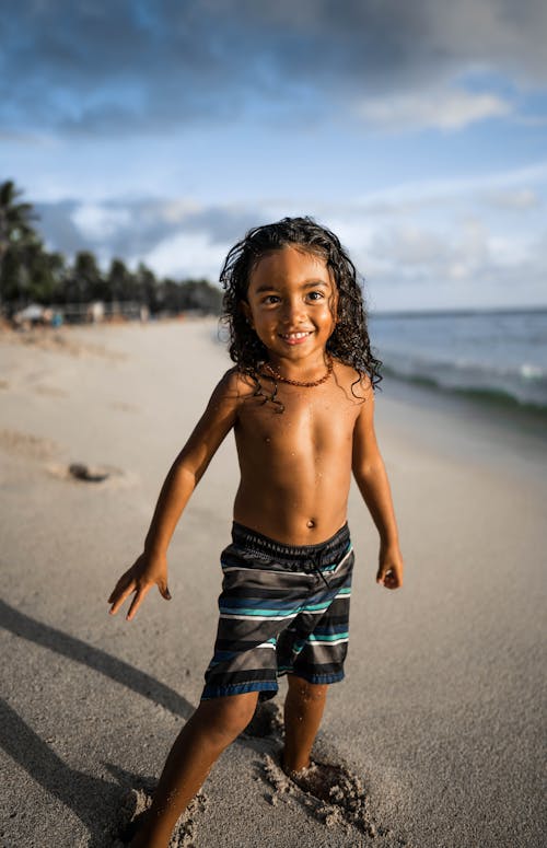 Free Topless Kid in Black and White Shorts Standing on Beach Stock Photo