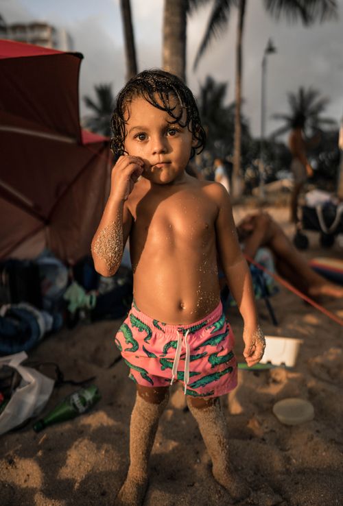 Free A young child with wet hair and sandy skin stands on a tropical beach surrounded by palm trees. Stock Photo