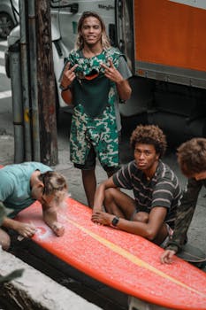 Group of young male surfers preparing surfboard on urban street, capturing outdoor adventure spirit.
