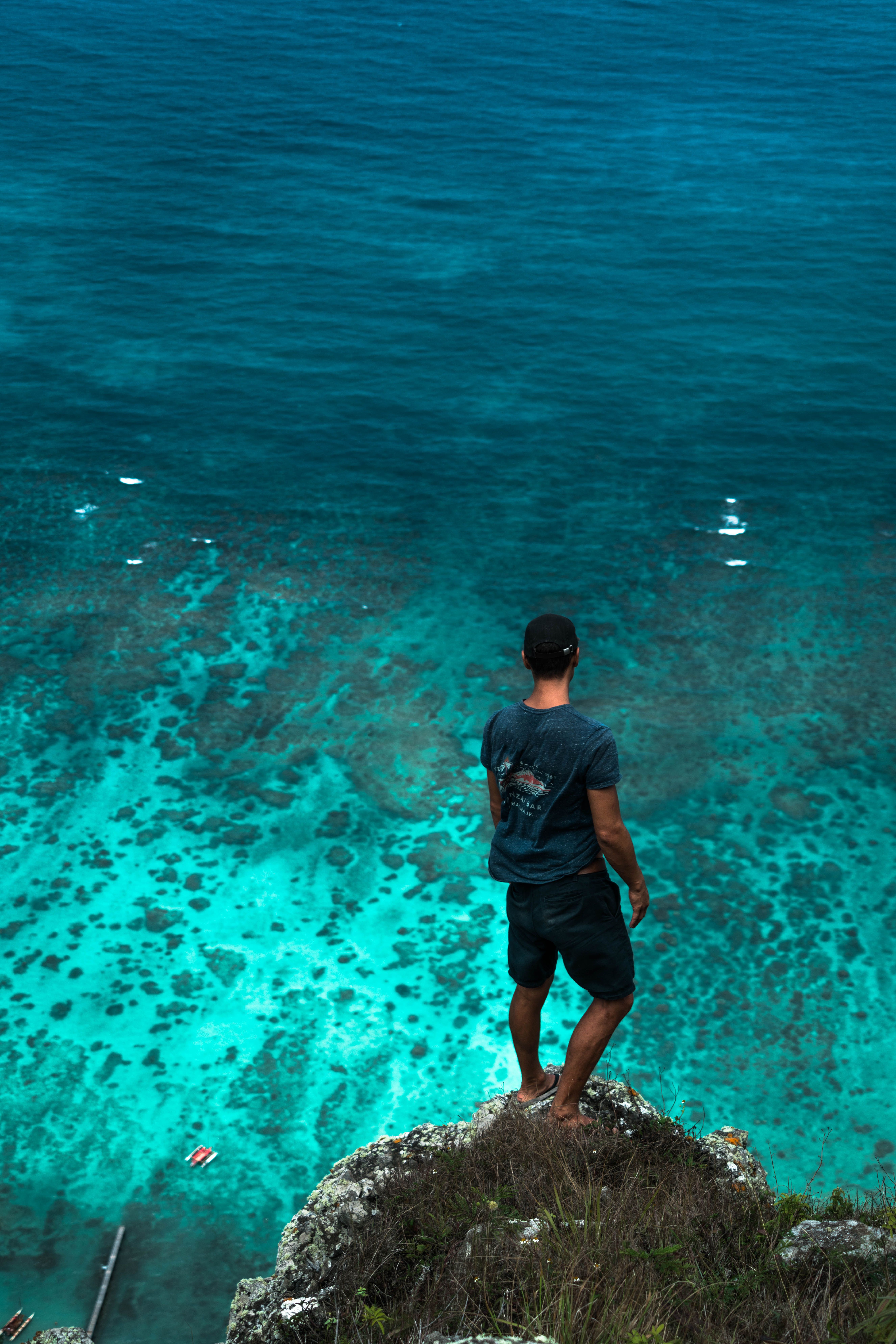 A man stands on a cliff edge gazing at the clear turquoise sea below, capturing a sense of adventure and freedom.