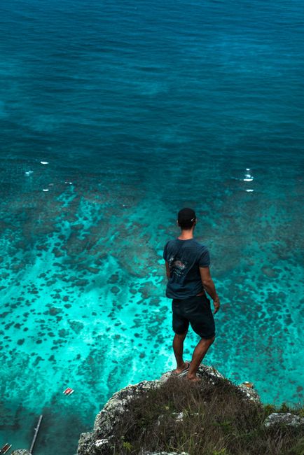 A man stands on a cliff edge gazing at the clear turquoise sea below, capturing a sense of adventure and freedom. A man stands on a cliff edge gazing at the clear turquoise sea below, capturing a sense of adventure and freedom.