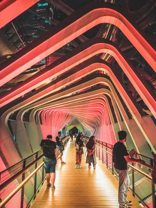 Free People walking on an illuminated pedestrian bridge in Jakarta, showcasing colorful architectural design. Stock Photo