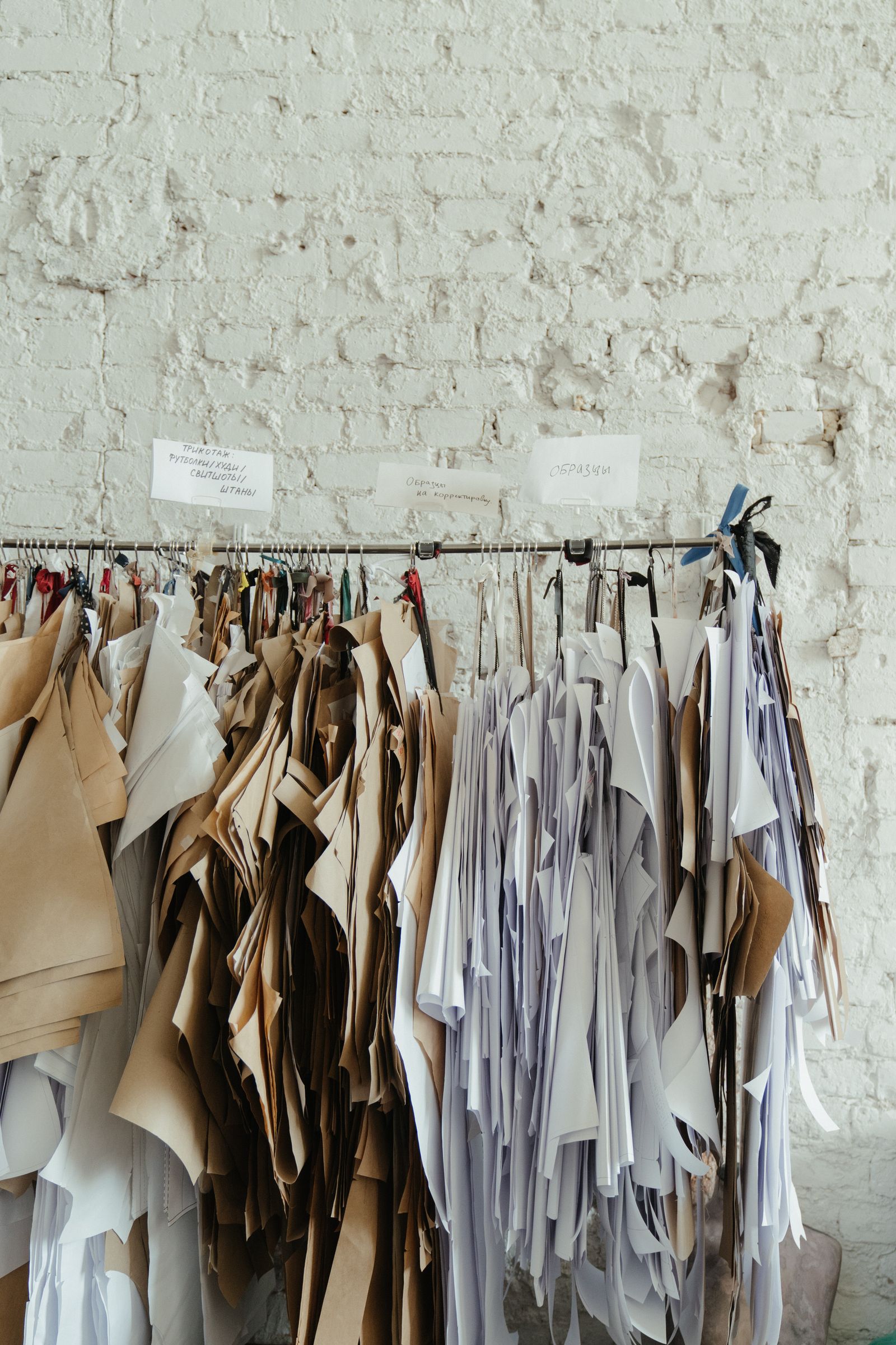 Clothing patterns and garments hanging on hangers against a textured wall without people