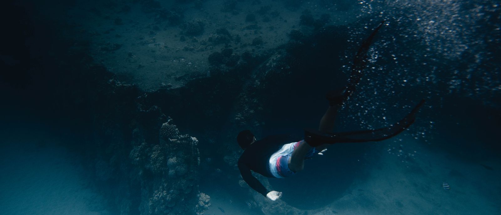 A diver swims gracefully through a vibrant coral reef underwater, captured in motion.
