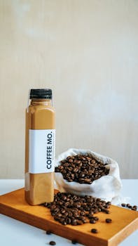 Composition of brewed aromatic cold coffee in plastic or glass bottle placed on wooden board near bag with organic coffee beans