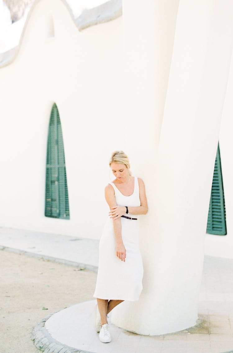 Woman In White Sleeveless Dress Leaning Against A White Concrete Post