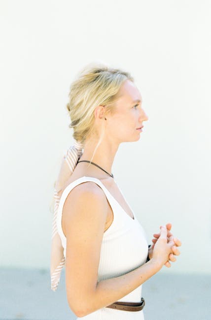Elegant side profile of a woman with blonde hair in a natural light setting, wearing a white tank top.