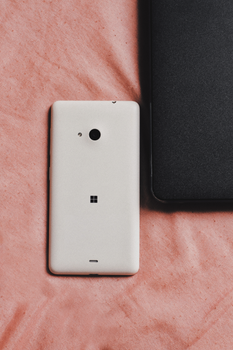 Close-up of a white smartphone and black tablet on a pink textile surface.