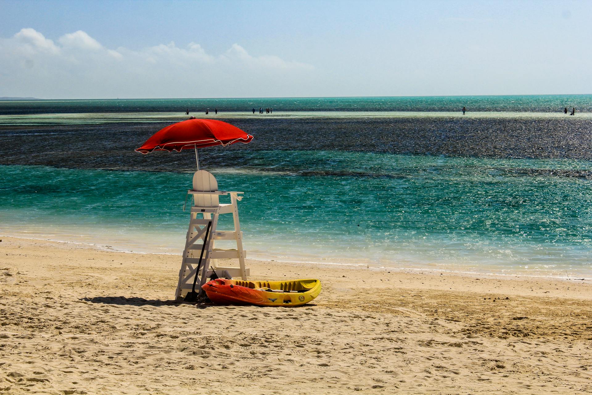 Peaceful beach in the Bahamas with a lifeguard chair, red umbrella, and kayak on the sand.